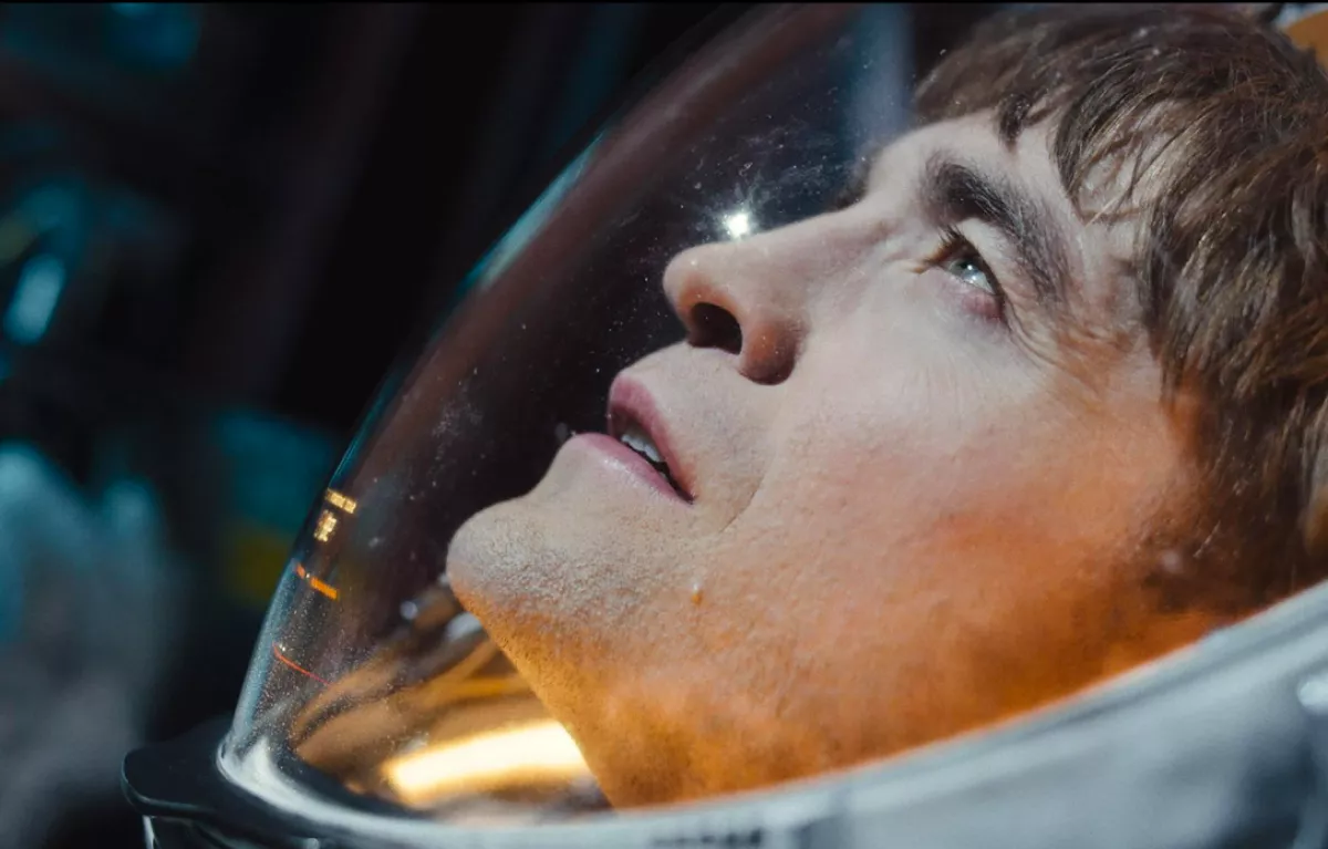 Foto del rostro de Robert Pattinson en la película "Mickey 17" usando un casco de astronauta y viendo hacia el cielo.