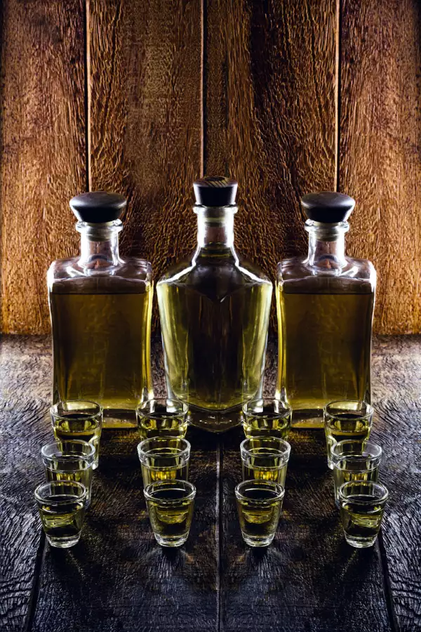 glass of alcoholic beverage, with bottle in the background, rustic setting. Brazilian gold type cachaça, called pinga.