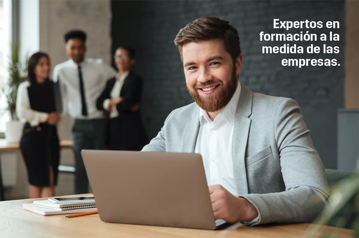 Hombre sonriendo y checando su laptop. Detrás se observan otras personas que lo están mirando.