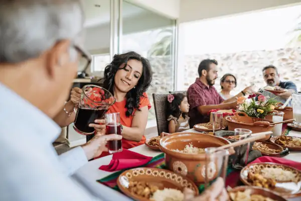 Tres hombres, dos mujeres y una niña alrededor de una mesa con cazuelas de barro, platos y agua de jamaica.jpg