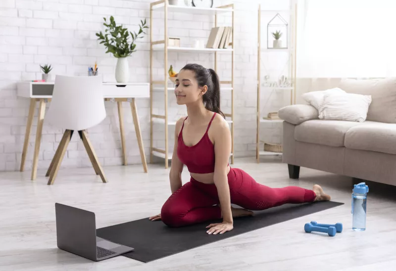 Hispanic girl exercising while watching online stretching course on laptop at home