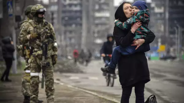 Una mujer sostiene y besa a un niño junto a soldados rusos en una calle de Mariupol el 12 de abril de 2022, mientras las tropas rusas intensifican una campaña para tomar la ciudad portuaria estratégica.