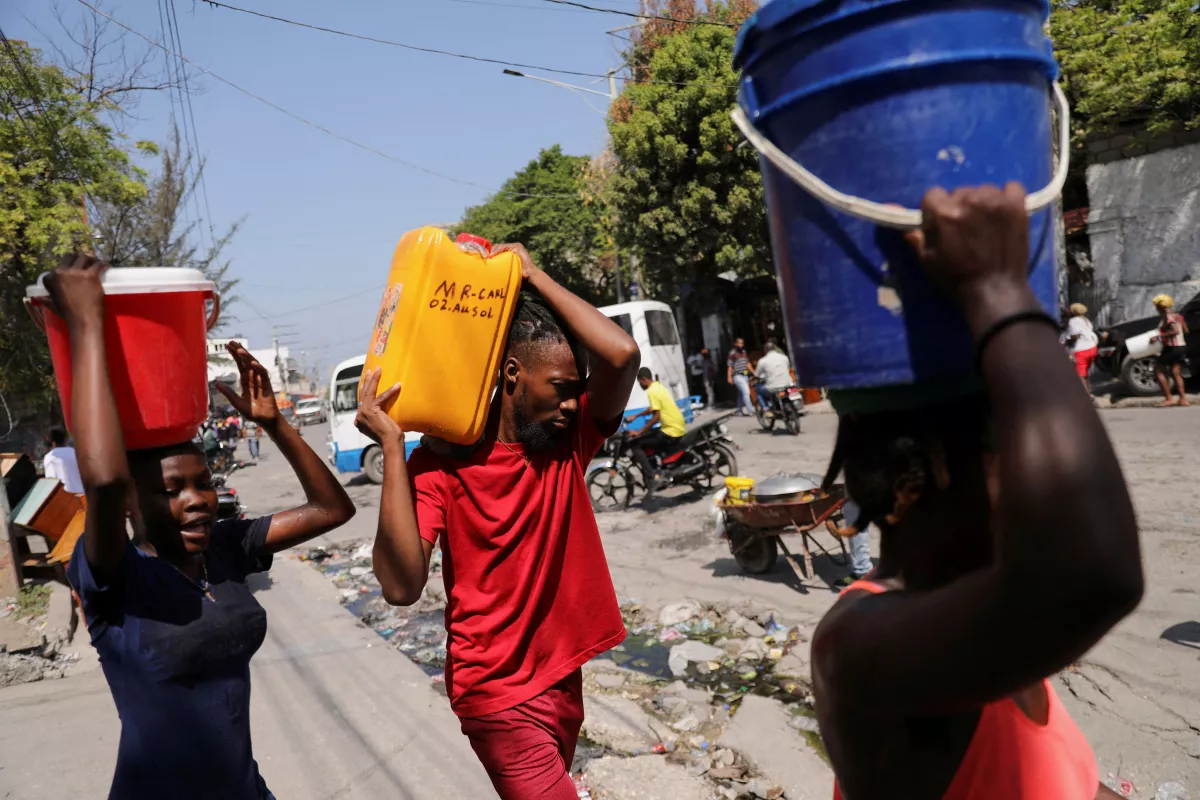 La gente lleva agua recogida en cubos y contenedores a lo largo de una calle después de que el primer ministro de Haití, Ariel Henry, se comprometiera a dimitir después de meses de escalada de la violencia de las pandillas, en Puerto Príncipe, Haití, el 12 de marzo de 2024.