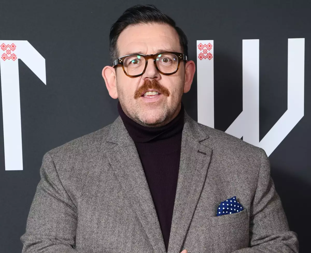 Foto del actor Nick Frost con lentes de pasta cafés, playera de cuello alto color vino y un saco con textura en tonos marrón.