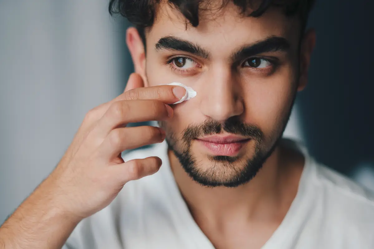 foto de un hombre untándose una crema para eliminar las ojeras alrededor de los ojos