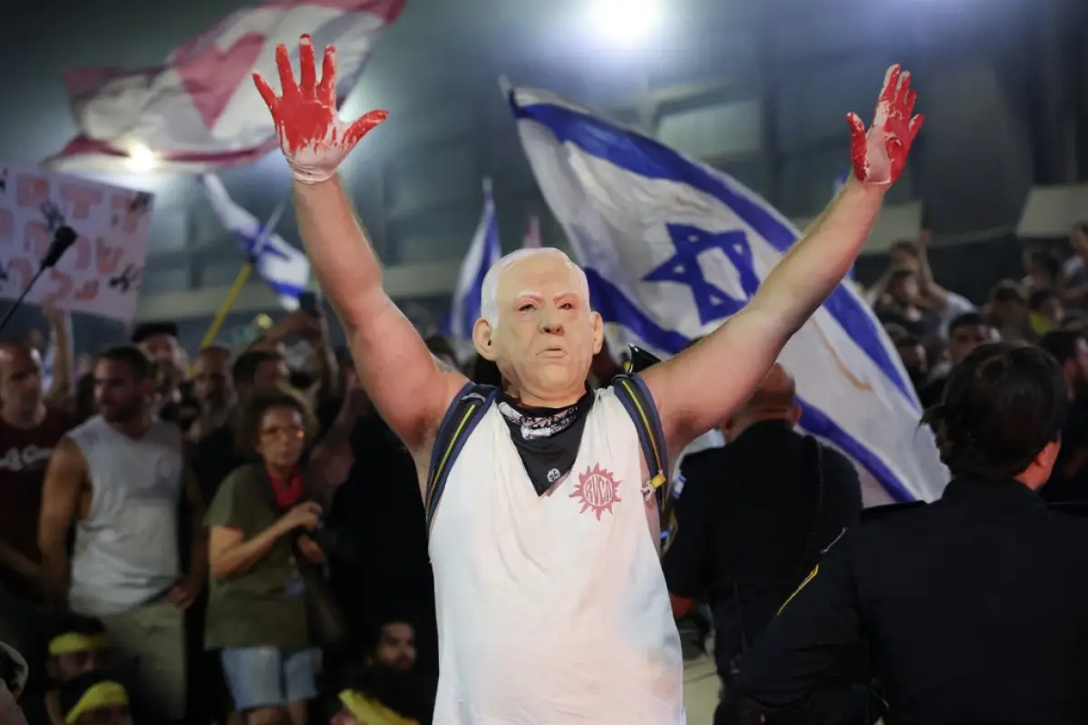 Un manifestante, con una máscara que representa al primer ministro de Israel, Benjamin Netanyahu, levanta las manos con guantes con pintura roja, durante una manifestación antigubernamental que pide la liberación de los israelíes retenidos como rehenes por militantes palestinos en Gaza desde octubre, en Tel Aviv el 1 de septiembre de 2024. 