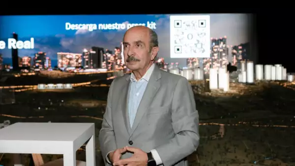 Hombre con saco gris y una imagen de una ciudad de fondo.