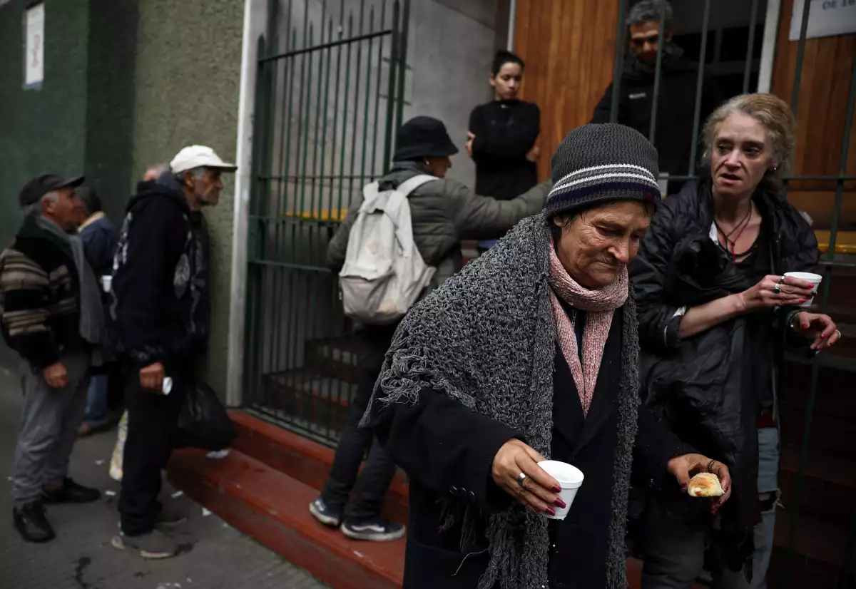 Una mujer se aleja después de recibir un refrigerio por la tarde de una iglesia que ayuda a los pobres, mientras otras personas se alinean, en Buenos Aires, Argentina, el 31 de mayo de 2024