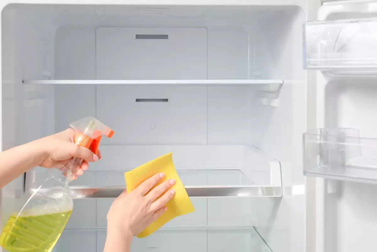 House cleaning - spray bottle with detergents for washing the fridge. Woman wipes the shelves of a clean refrigerator