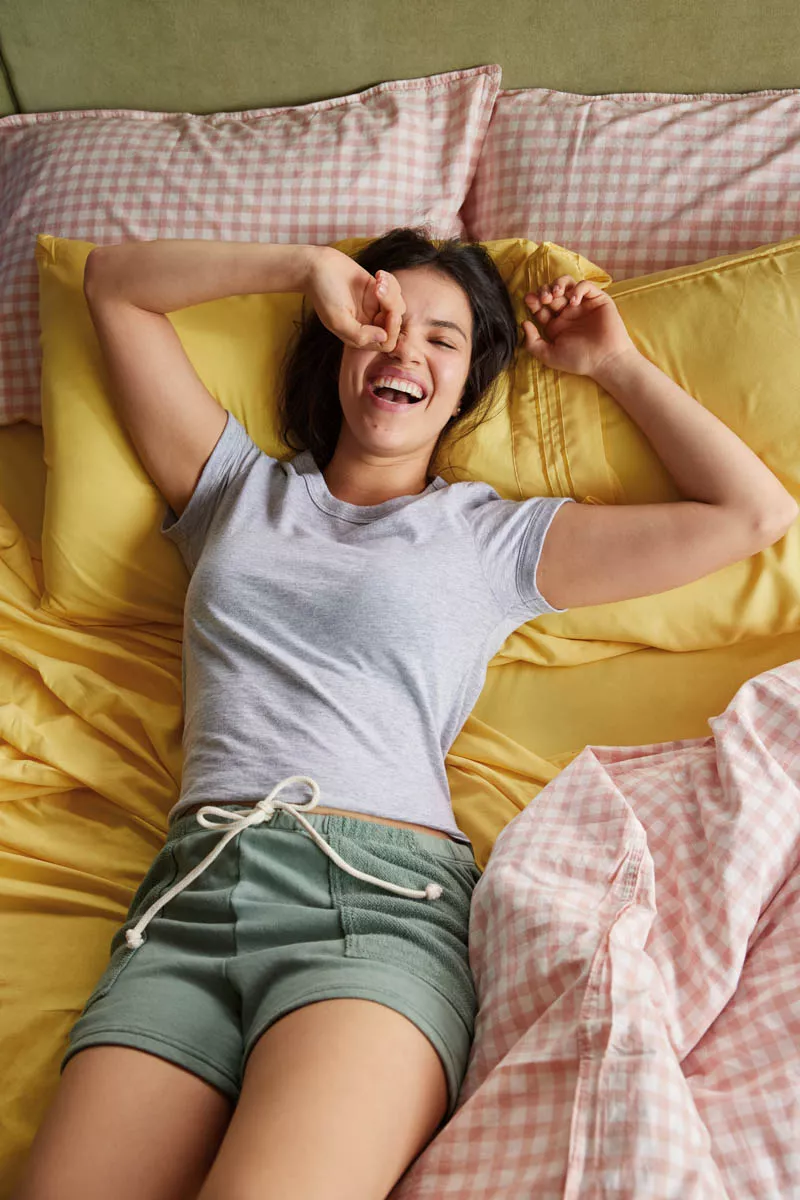 Chica acostada en cama con shorts verdes y playera gris
