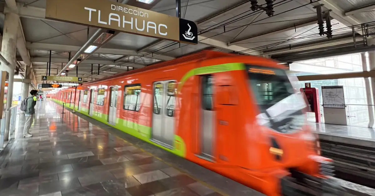 Un tren de color naranja con vivos verdes con un letreo que dice Tláhuac, una persona en el anden.jpg