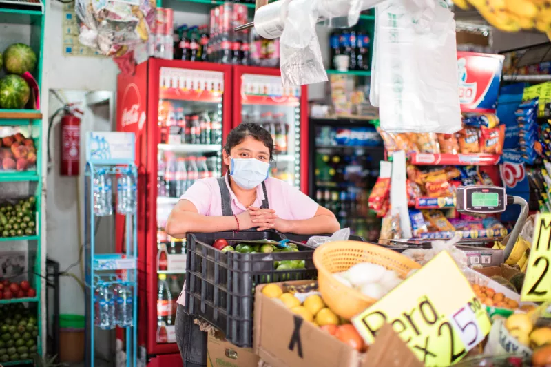Una mujer con cubrebocas atiende un pequeño establecimiento comercial