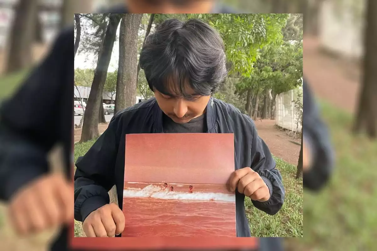 Foto del músico mexicano Macario Martínez sosteniendo entre las manos una foto en tonos sepia de una playa.