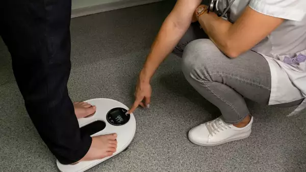 Una mujer pesándose frente una médico. 