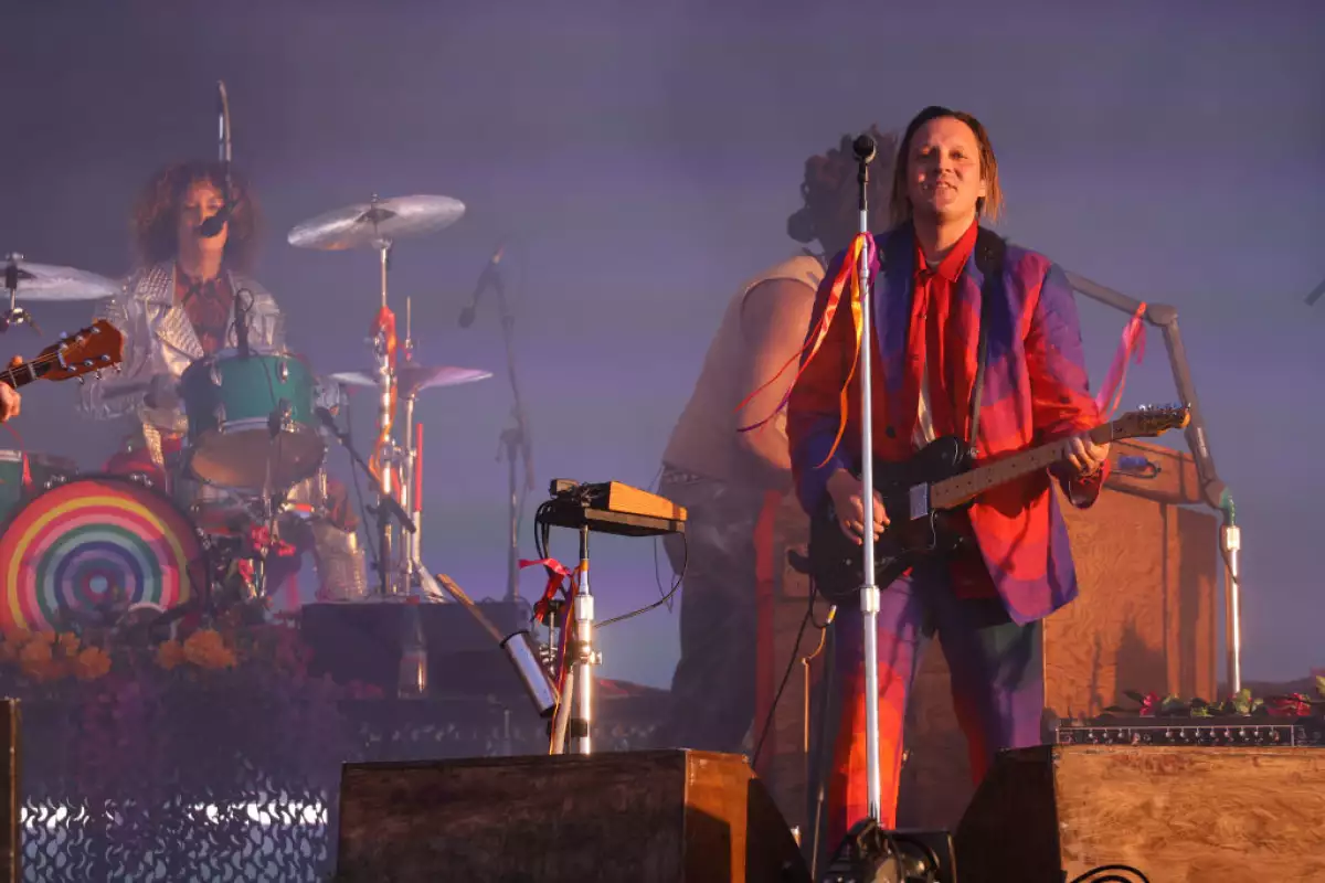 Foto de Win Butler con un saco de colores rojos y morados y la guitarra en la mano cantando durante un concierto en Chile.