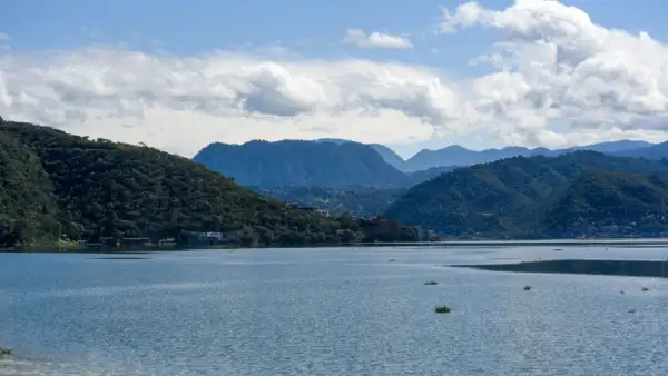 Un cuerpo de agua rodeada de tres montañas de color verde bajo un cielo con nubes blancas.jpg