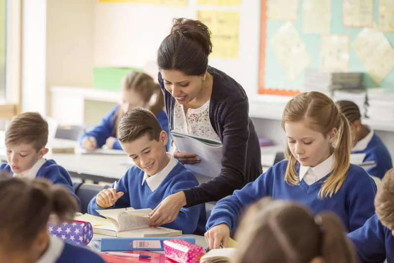 Profesora de primaria muestra una página de un libro a un niño vestido con un suéter azul. 