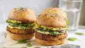 Healthy baked sweet potato burger with whole grain bun, guacamole, vegan mayonnaise and vegetables on a wooden board. Vegetarian food concept, light background.