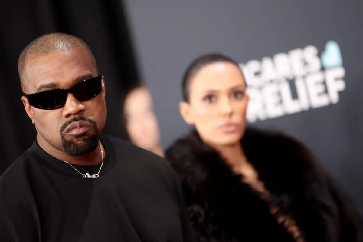 Foto de Kanye West vestido de negro con lentes oscuros y detrás de él la arquitecta Bianca Censori, con quien está casado desde hace cuatro años.