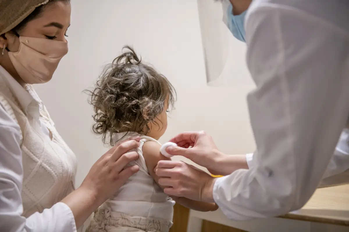 Un médico está limpiando el brazo de una niña pequeña con un poco de algodón en preparación para administrar la vacuna contra la COVID-19.