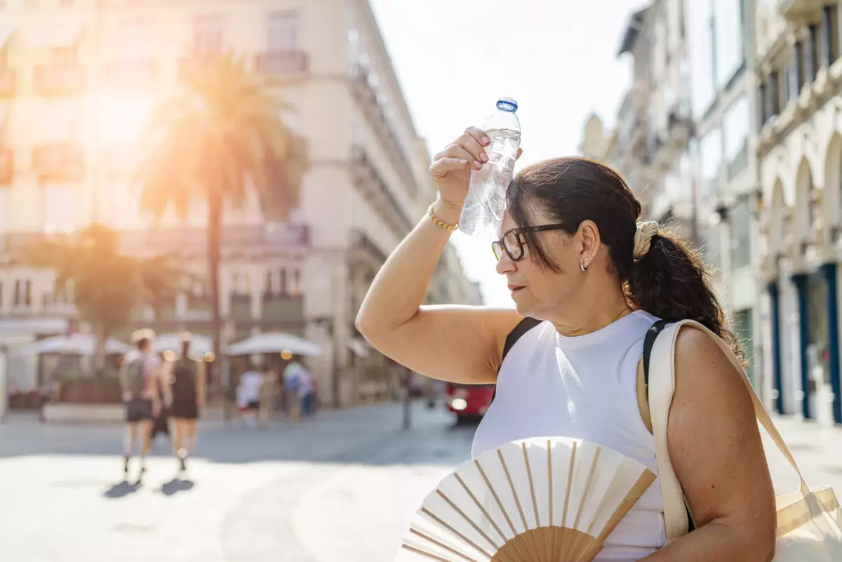 Woman tourist walking by the city in a sunny summer day suffering from high temperatures, heat stroke and dehydratation
