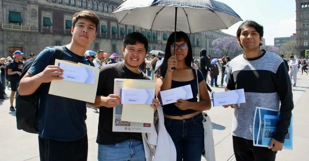 Tres hombres yuna mujer joven que muestran un sobre. Están en la plancha del Zócalo de la CDMX bajo el sol.jpg