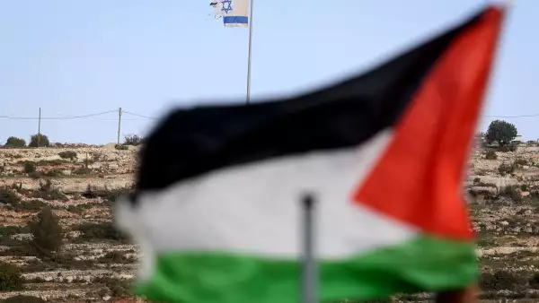 Esta foto tomada desde la aldea de Umm Safa, al norte de Ramallah en la Cisjordania ocupada, muestra una bandera palestina (en primer plano) y una bandera israelí ondeando en la cima de una colina con vistas al pueblo el 16 de febrero de 2026. El gobierno de Israel ha aprobado un proceso para registrar la tierra en Cisjordania como "propiedad estatal", lo que provocó la condena de las naciones árabes y los críticos que dijeron que aceleraría la anexión del territorio palestino.