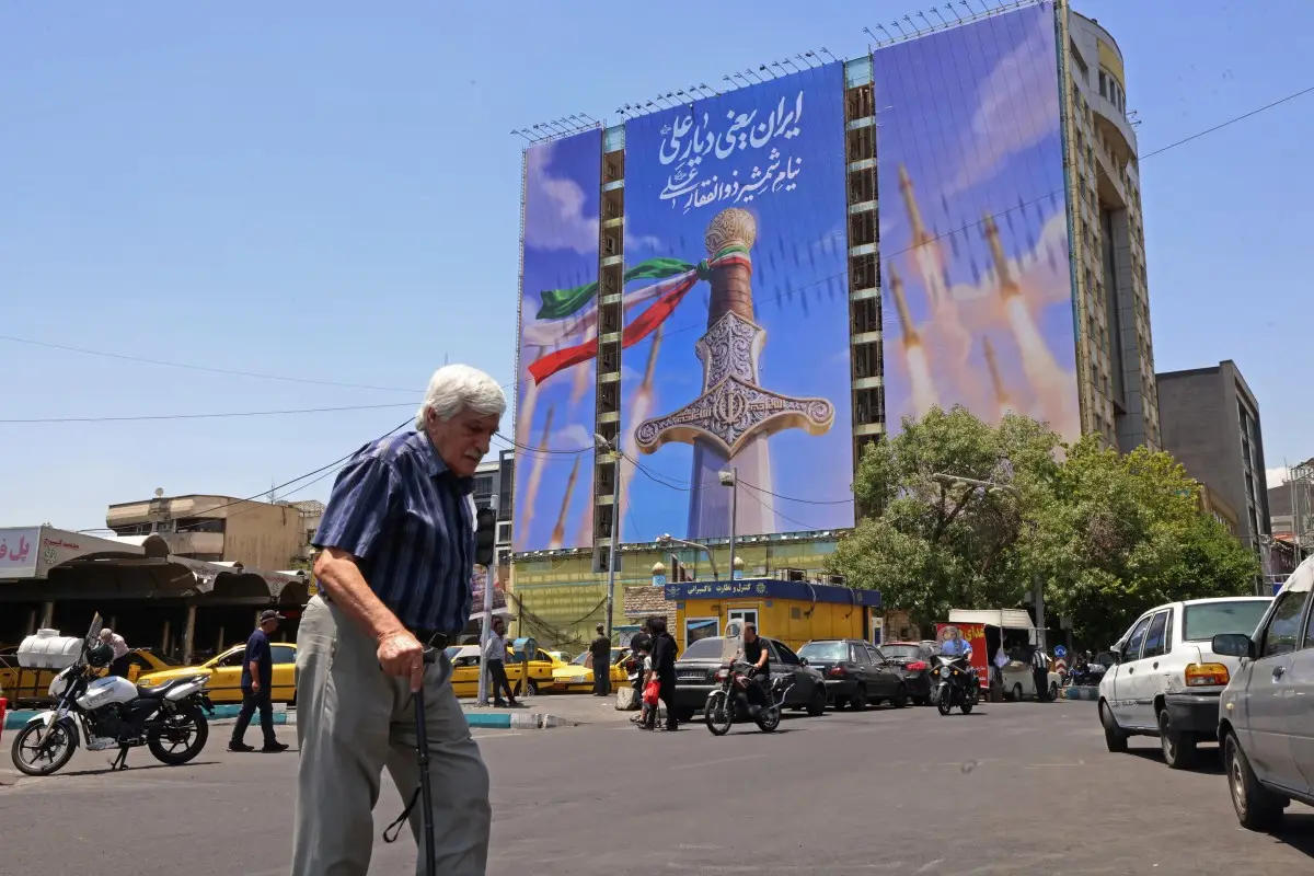 Un hombre pasa junto a una pancarta gigante que representa misiles iraníes y una espada perteneciente al Imam Ali, el primer imán de los chiítas, en la plaza Vanak en Teherán el 10 de junio de 2026. El Ministerio de Relaciones Exteriores de Irán dijo el 10 de junio que Estados Unidos había dañado el esfuerzo diplomático internacional en curso para poner fin a la guerra, después de más ataques estadounidenses contra objetivos en el sur de Irán.