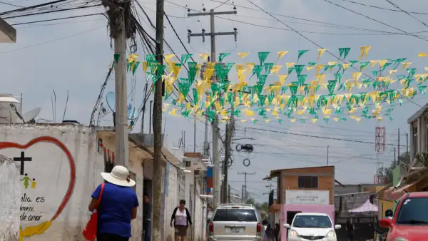 Una calle en donde se observan cables de luz, una camioneta, un coche blanco y uno rojo