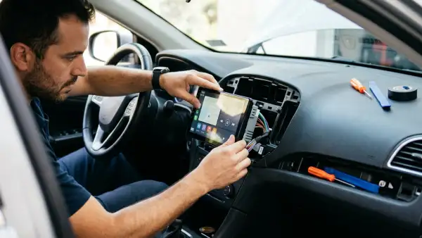 Hombre instalando una nueva pantalla en la parte frontal del carro. Estas pantallas suelen funcionar para controlar el infoentretenimiento.