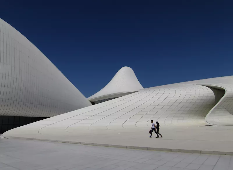 Two people walk across the plaza at the Zaha Hadid designed Heydar Aliyev Center in Baku, Azerbaijan