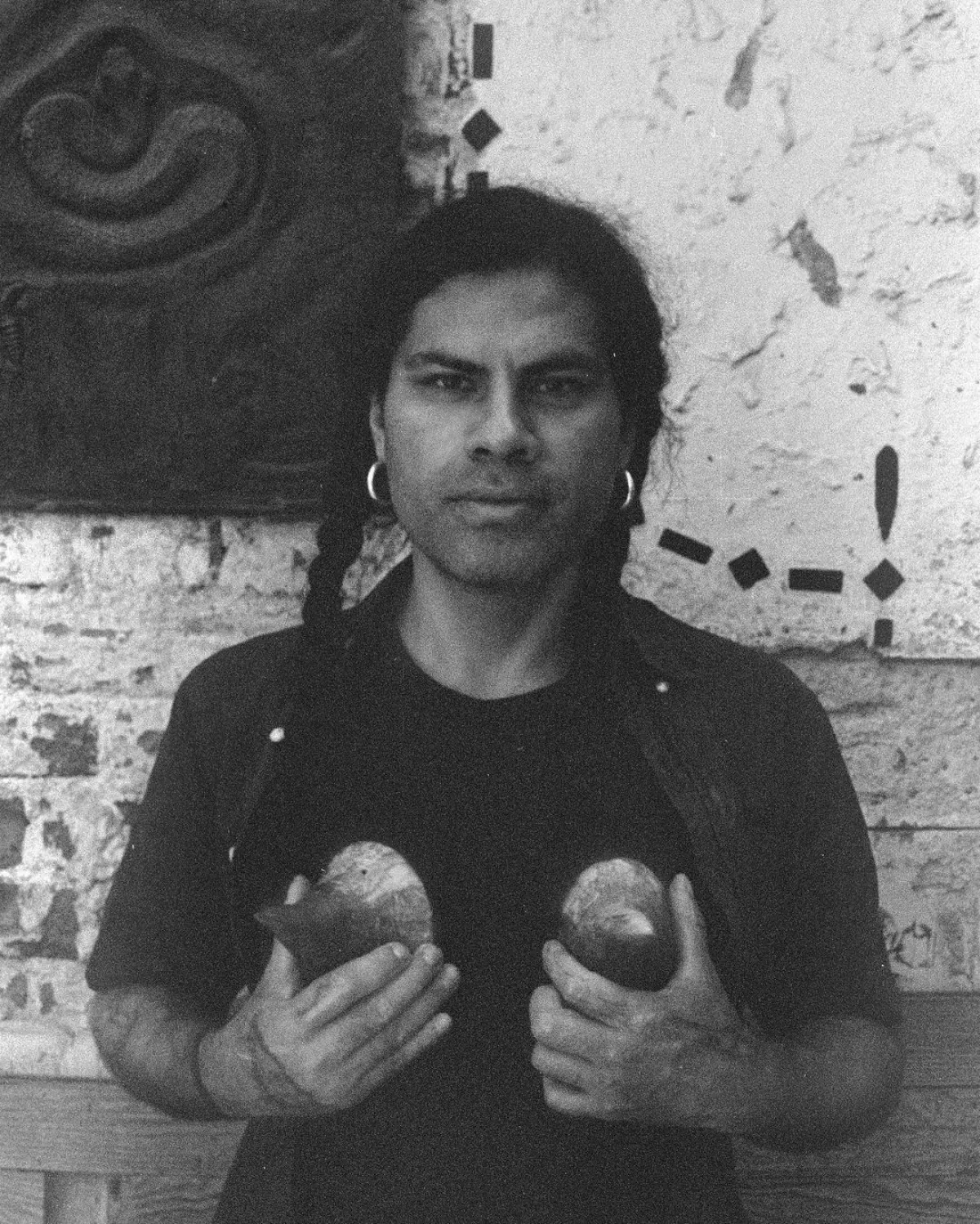 Foto en blanco y negro del artista Chavis Mármol sosteniendo un par de esculturas.