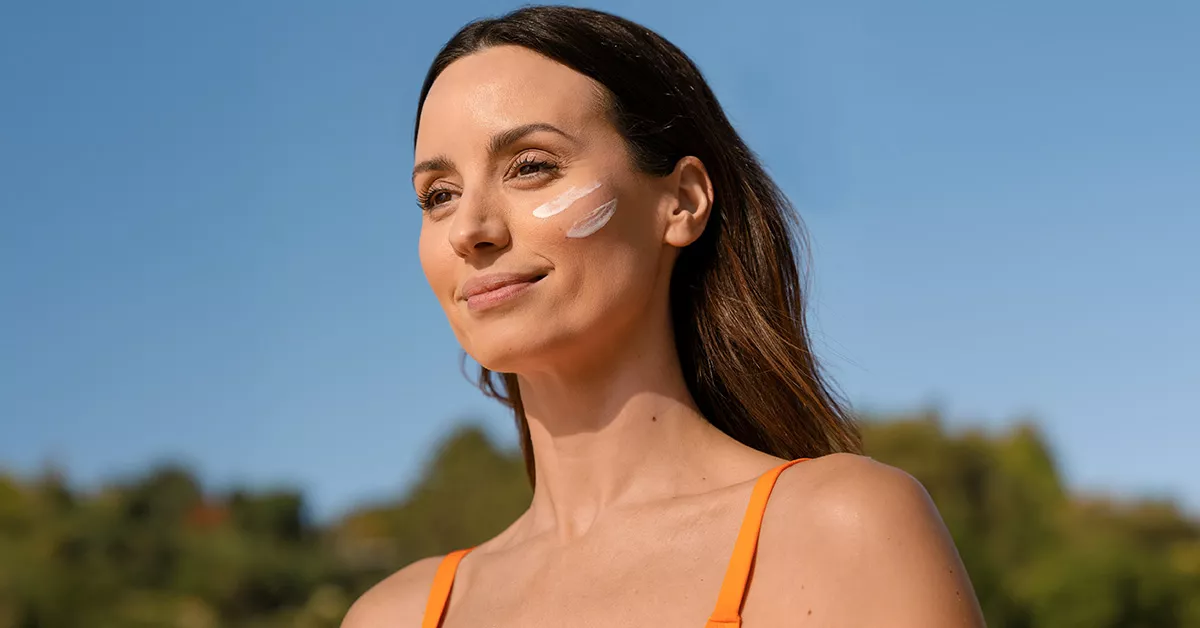 close up a un amujer sonriendo a la cámara, mientas sostiene en la mano un bote de ISDIN bloqueador solar