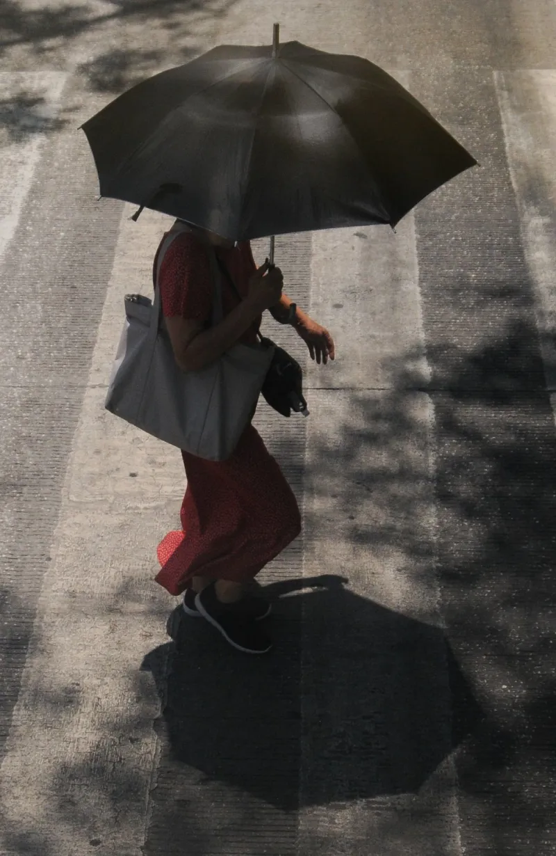 Una mujer cruza la calle protegiendose del sol con una sombrilla.