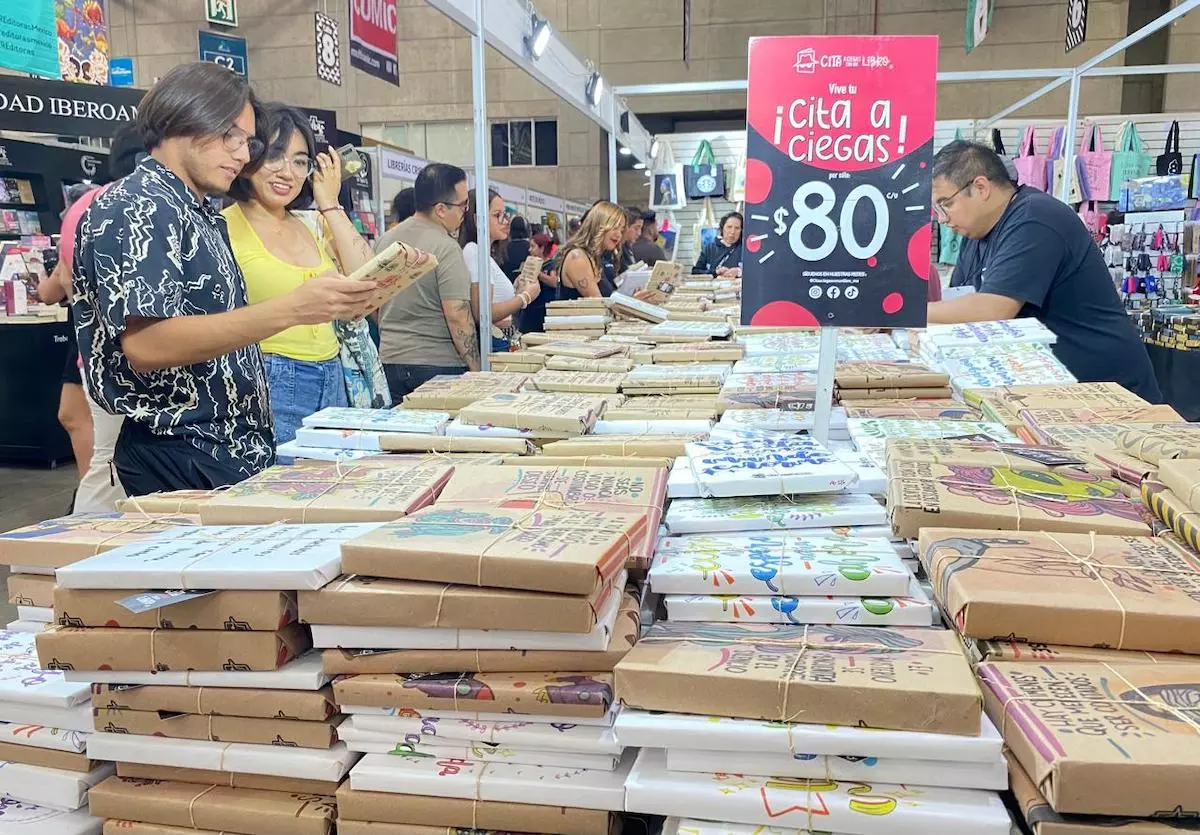 Imagen de jóvenes revisando los libros a la venta en uno de los 250 locales de expositores de la Feria Nacional del Libro de León 2025. 