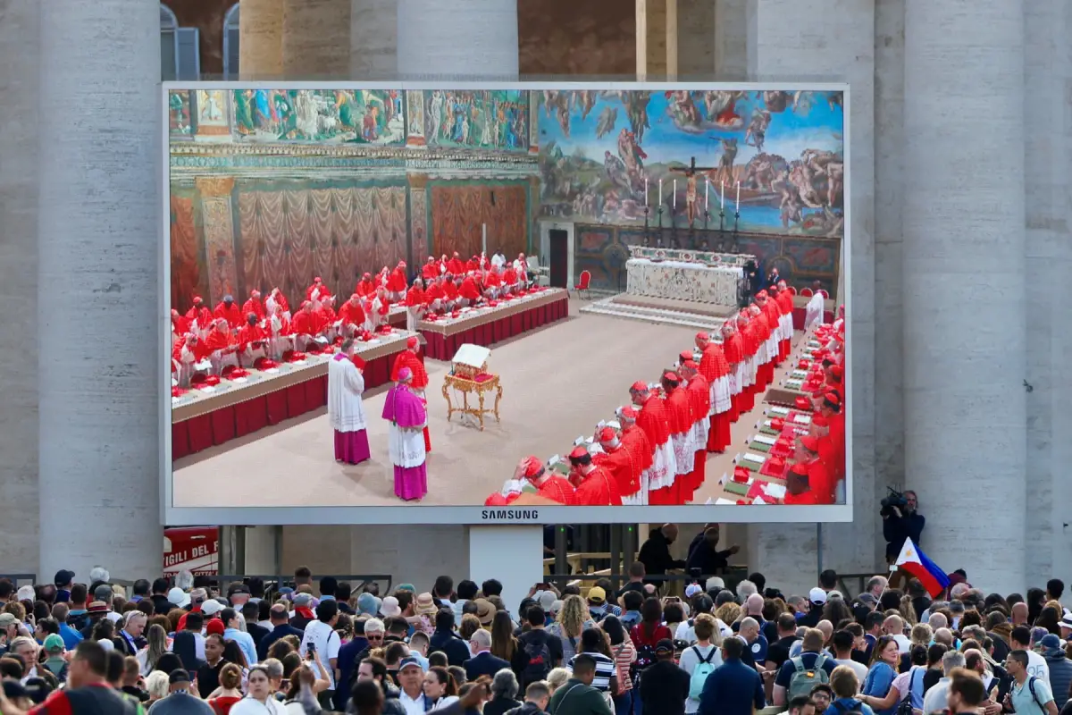 La gente mira una pantalla en la Plaza de San Pedro que muestra a los cardenales en la Capilla Sixtina, el primer día del cónclave para elegir al siguiente Papa, visto desde Roma, Italia, el 7 de mayo de 2025.