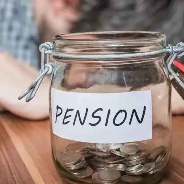 Persona recostada sobre una mesa y un tarro de vidrio con monedas y el emblema pensión.