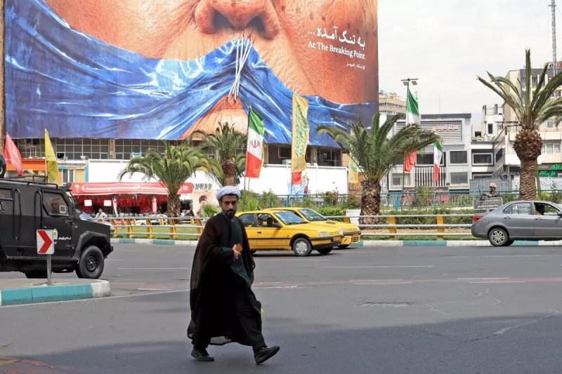 Un clérigo iraní pasa junto a una valla publicitaria antiestadounidense que se refiere al presidente Donald Trump y al estrecho de Ormuz, instalada en un edificio en la plaza Valiasr en Teherán el 2 de mayo de 2026.