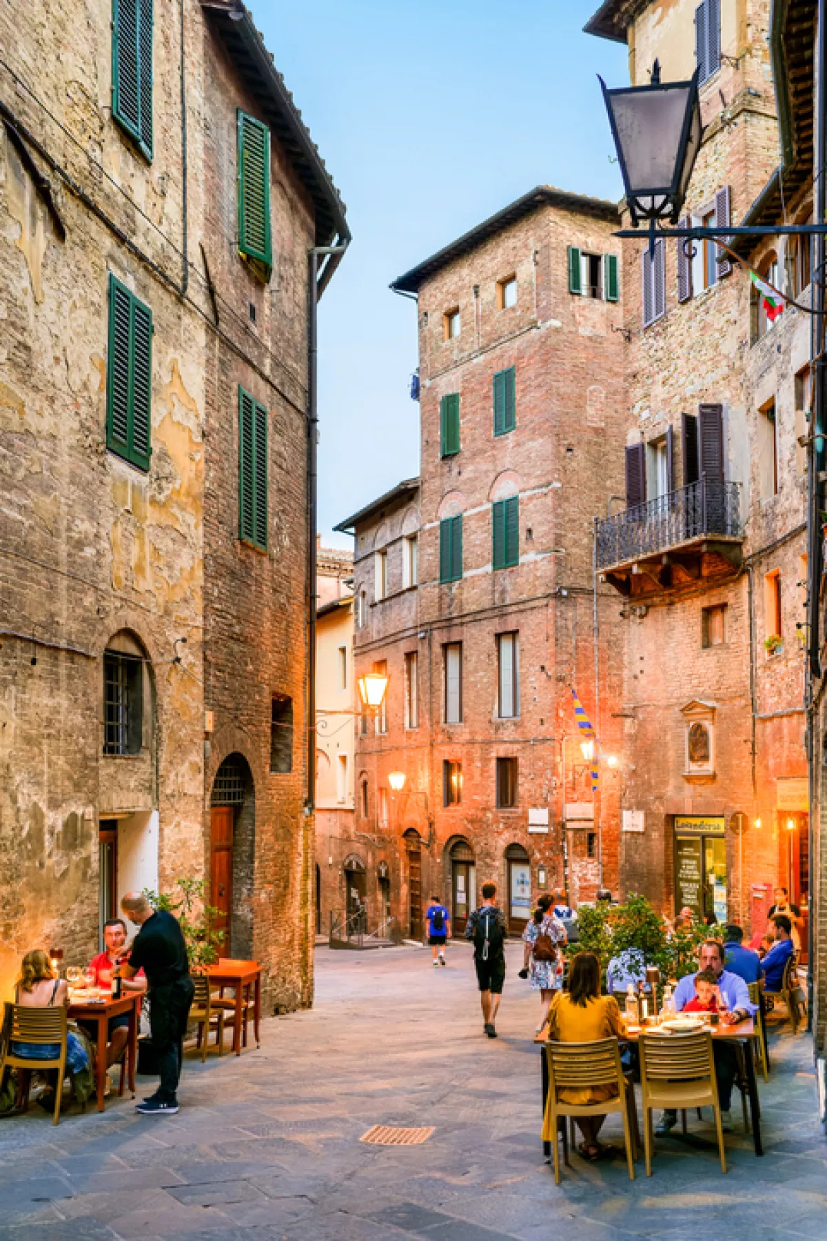 Some tourists enjoy life in a restaurant along a beautiful stone alley in the medieval heart of Siena in Tuscany