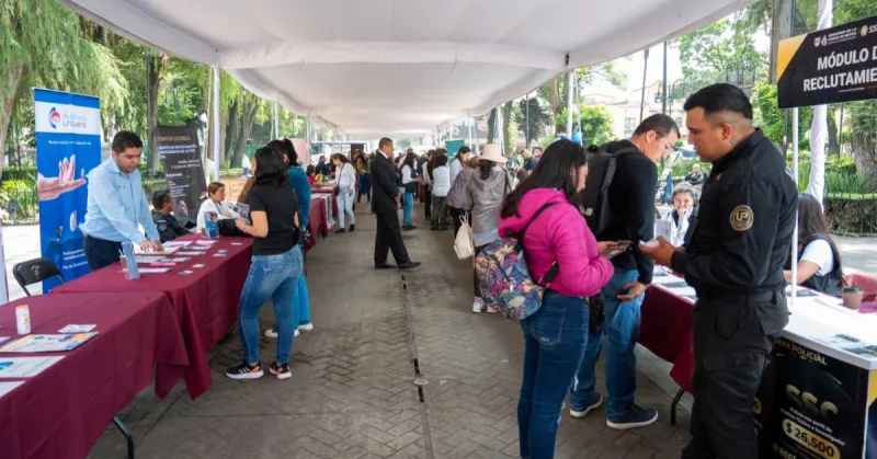 Un pasillo largo al aire libre con mesas al lado y mujeres y hombres hablando, traen folletos en la mano .jpg