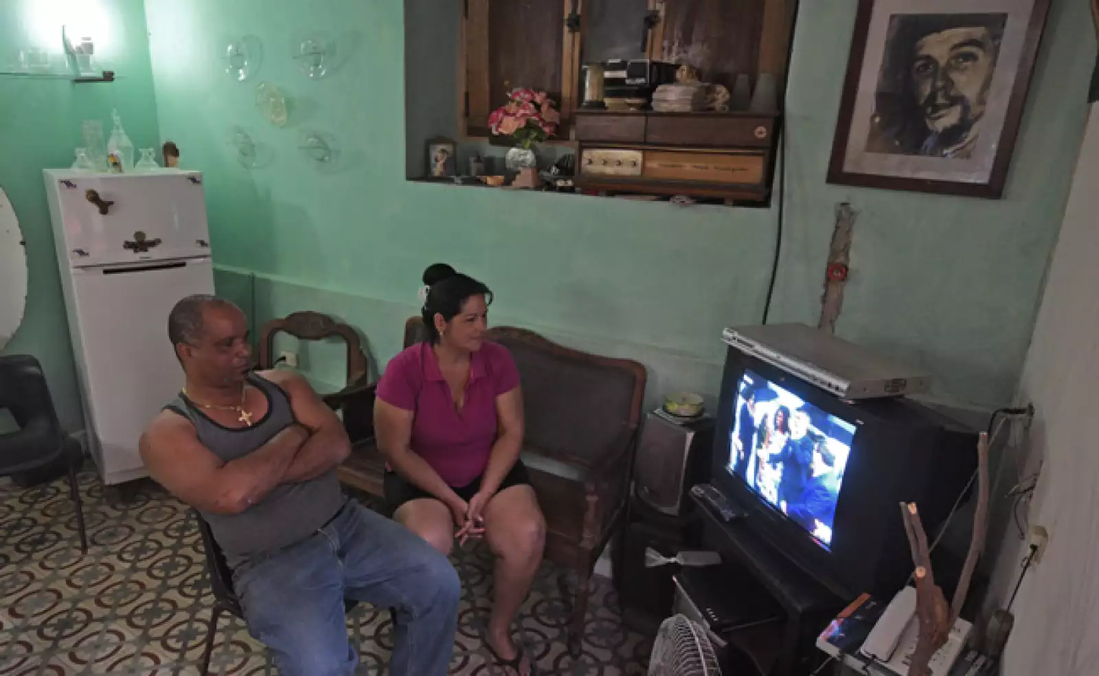 Una pareja de cubanos, acompañados por el retraro del Che Guevara, ven la transmisión de la televisión estatal
