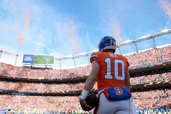 Foto de Bo Nix de espalda entrando al estadio de los Broncos y unas gradas completamente anaranjadas, como el color del equipo de Denver