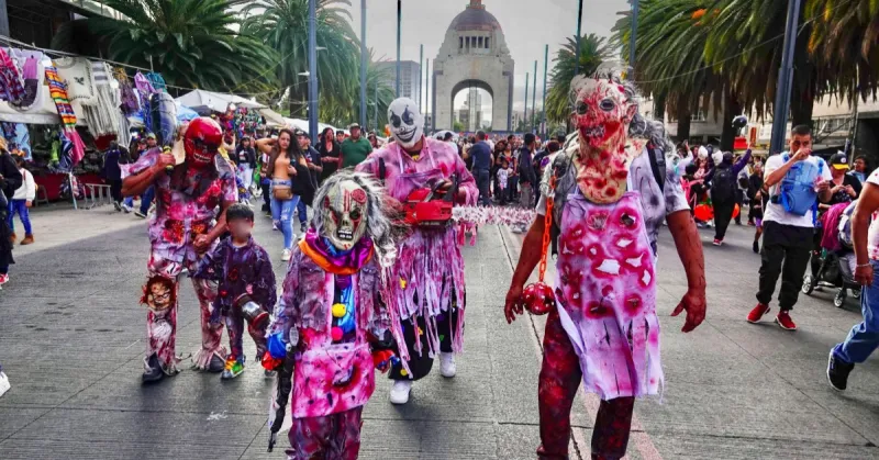 Tres adultos y dos niños con batas y máscaras de látex llenas de sangre caminando por avenida Revolución.jpg