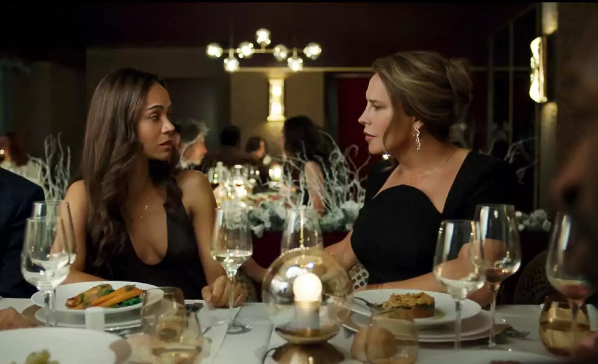 Foto de una escena de la película 'Emilia Pérez', con Zoë Saldaña y Karla Sofía Gascón sentadas en una mesa de restaurante mirándose frente a frente.