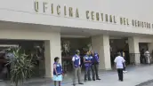 Fachada de edificio color beige con letras de "Oficina Central del registro Civil" y cuatro hombres y una mujer con chaleco azul .jpg