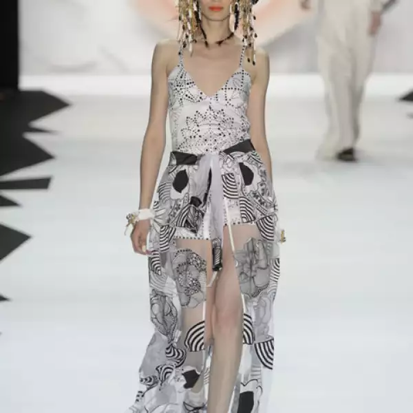 Jumpsuit blanco de satín con aplicaciones de jacquard, túnica de patchwork usada como falda y sandalias de plataforma.