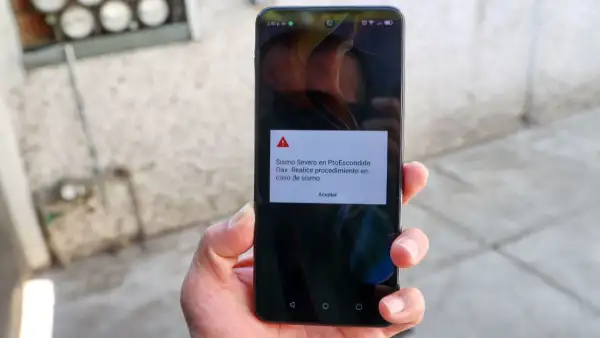 La mano izquierda de una personas sostiene un teléfono celular en donde suena la alerta sísmica.jpg