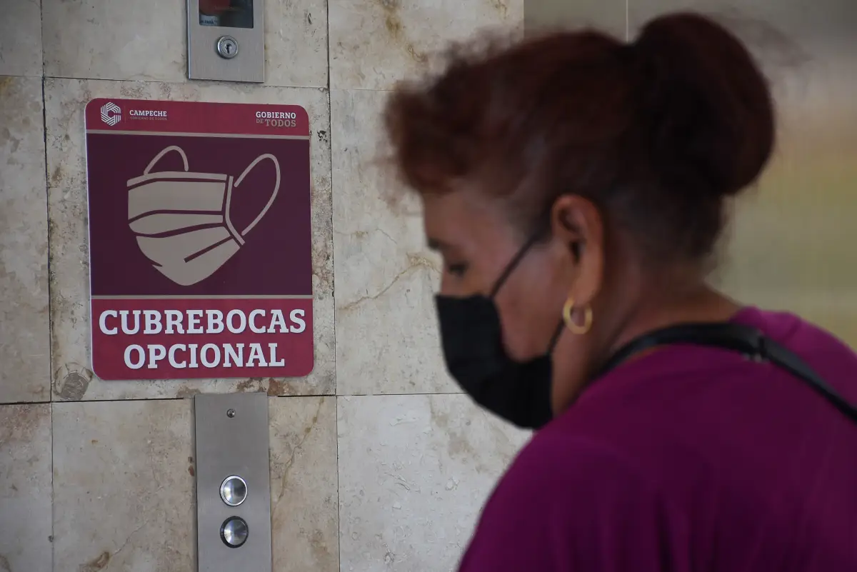 Mujer con cubrebocas bien colocado, frente a un aviso de que su uso es opcional. 
