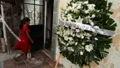 Niña con vestido rojo y botas camina frente a una casa junto a una corona funeraria con un mensaje de familiares de personas desaparecidas.