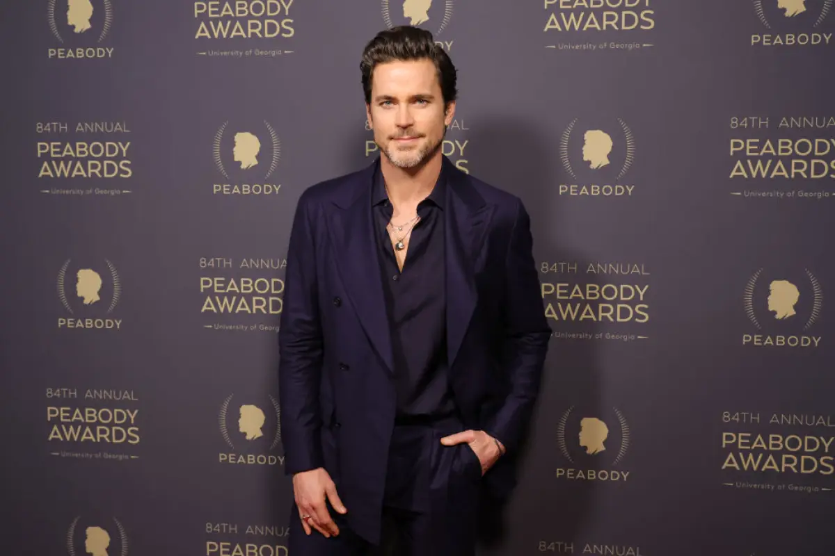 Matt Bomer en los Peabody Awards vistiendo un traje oscuro y una camisa negra desabotonada.